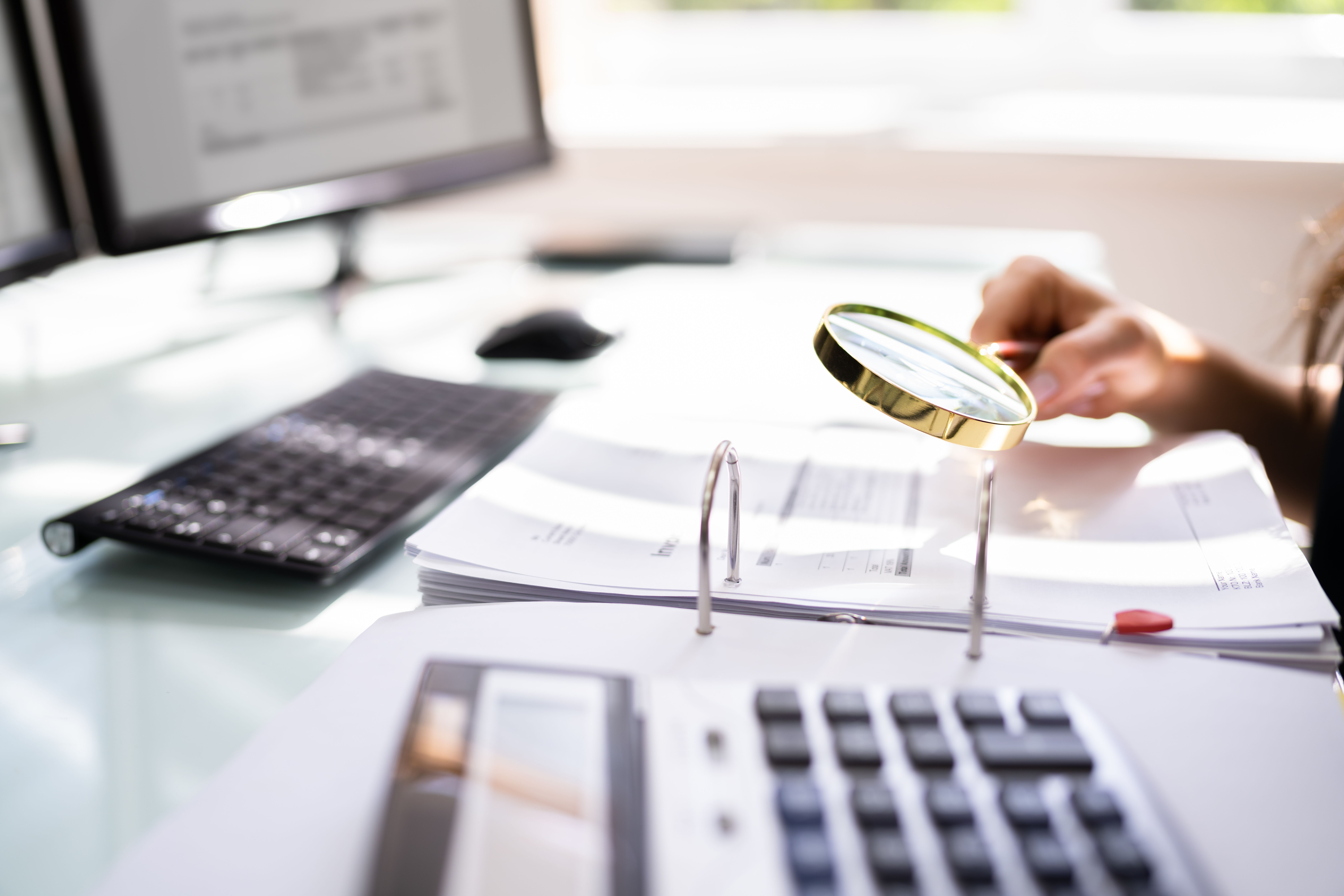 Person holding magnifying glass over business reports